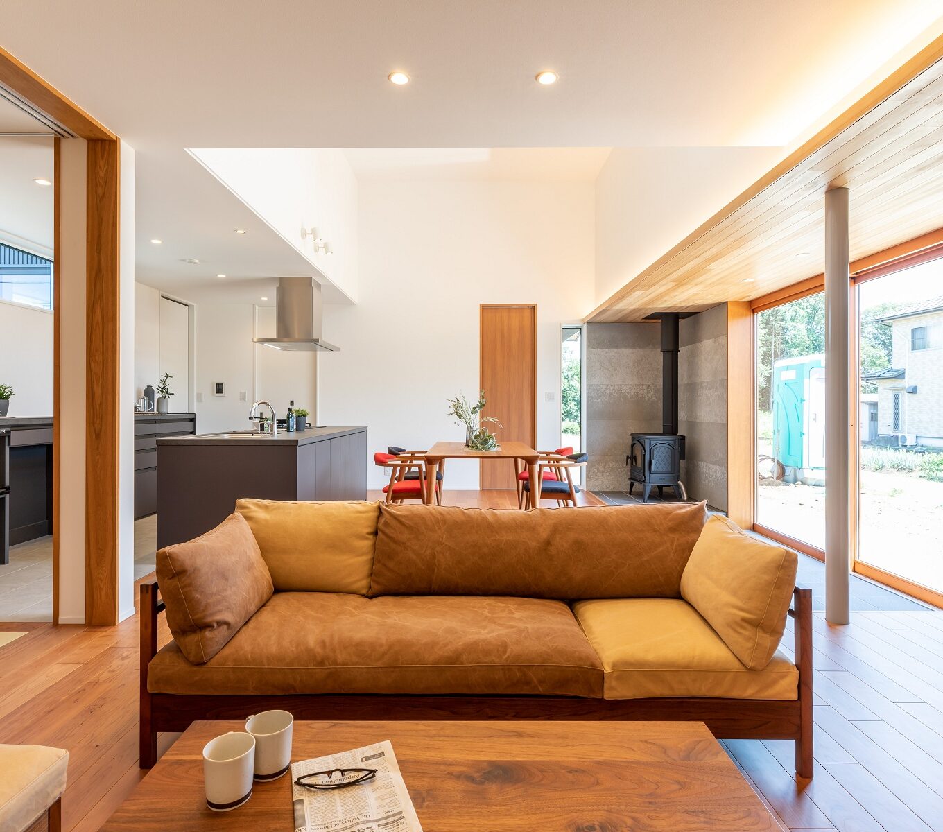 天井と同じく外と内をつながるようにつくられた、タイル土間に薪ストーブ。 広く大きいLDKに映える、あたたかみのある木製の大型サッシ。