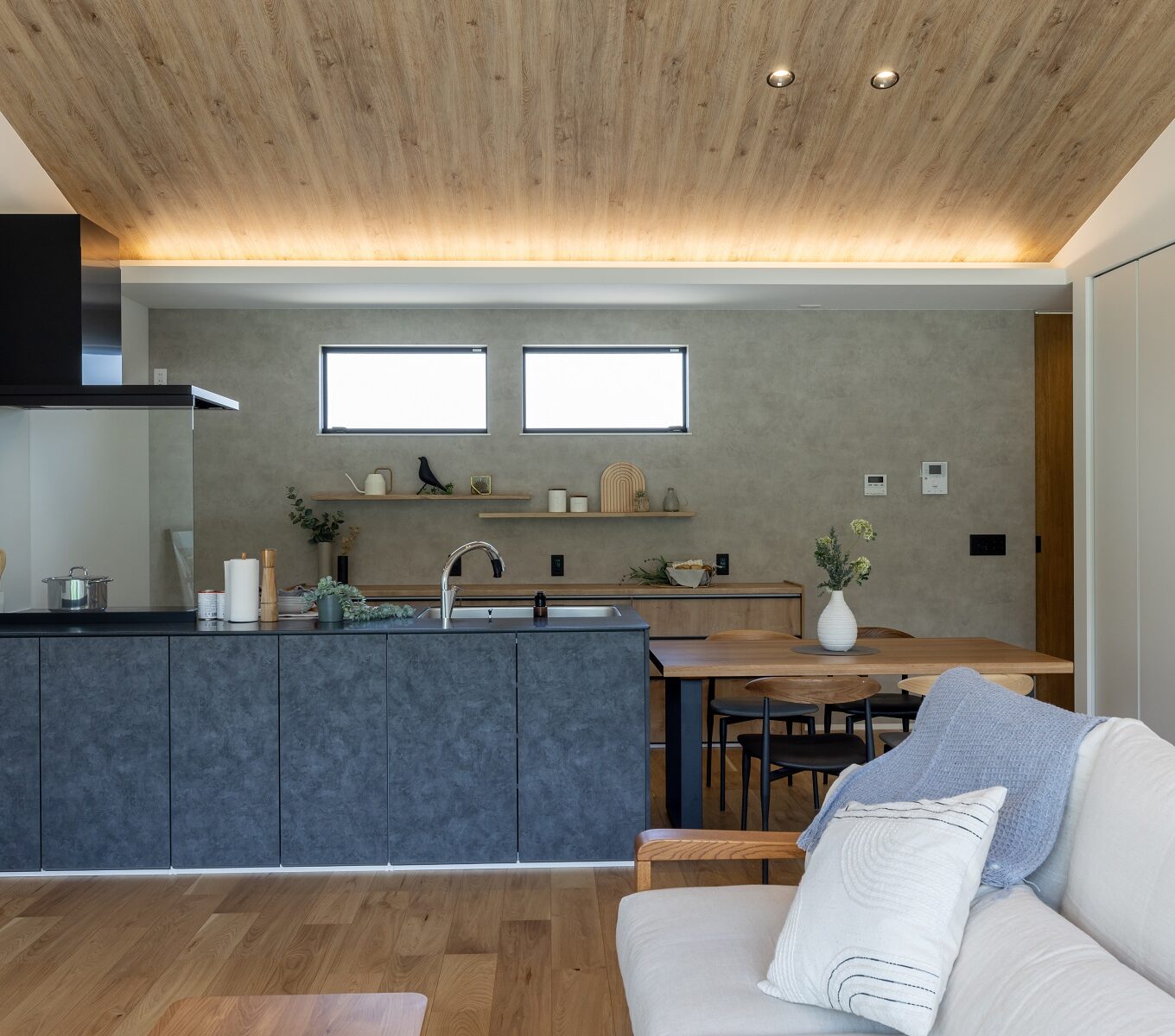 カップボードと飾り棚は、ＬＤＫの雰囲気に合わせ木目柄を取りいれ柔らかい印象に。 ダイニングテーブルはキッチンと横並びにし動線をコンパクトに。 木目柄で揃えたことで、ブラックのオープンキッチンの美しさを際立たせました。