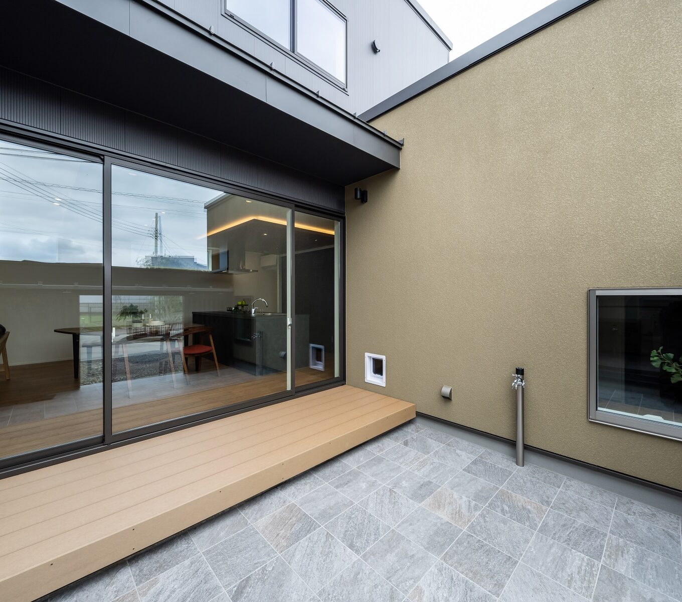 ３方をコの字型の建物に囲まれた中庭は、 光を採り込みつつプライバシーを守ります。 中庭にはリビングから続くタイルデッキがあり、セカンドリビングとして機能します。 そこへは大切な家族の一員であるである猫ちゃんたちも一緒に居られるように、 猫専用のペットドアを設け、愛猫が室内と中庭を安全に自由に行き来できる設計としました。  